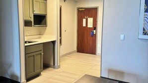Une chambre d’hôtel avec une kitchenette, une porte en bois, une petite table et un tapis à motifs.