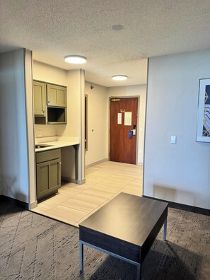 Une chambre d’hôtel avec une kitchenette, une porte en bois, une petite table et un tapis à motifs.