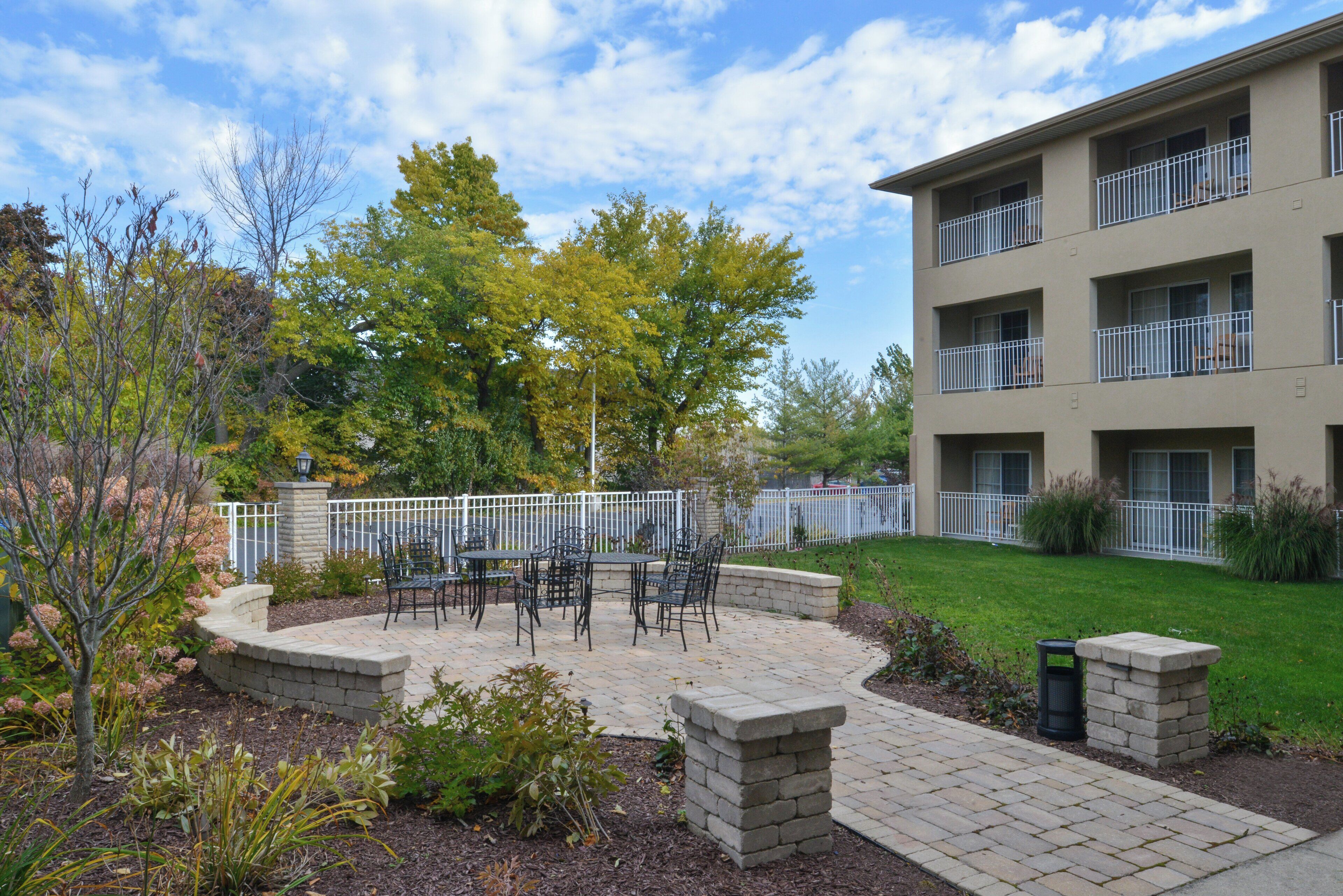A courtyard with outdoor seating, a stone wall, and a multi-story building with balconies.