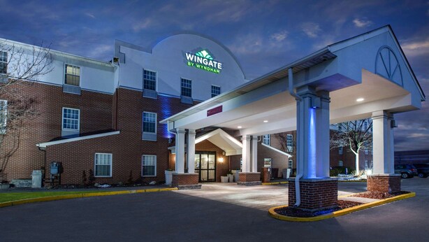 A Wingate by Wyndham hotel with a prominent entrance, brick facade, and a covered parking area. - Wingate by Wyndham Roseville/Detroit (Roseville)