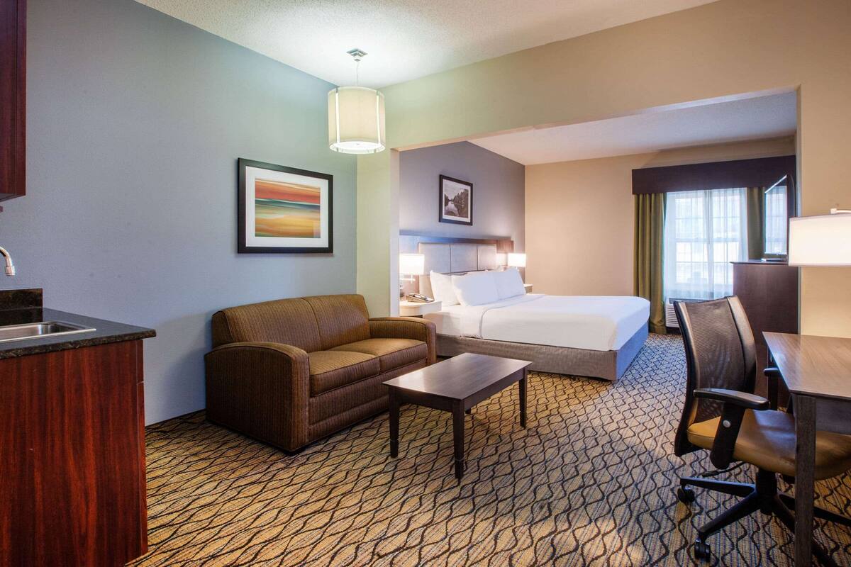 A hotel room with a bed, a sofa, a desk, and a kitchenette.