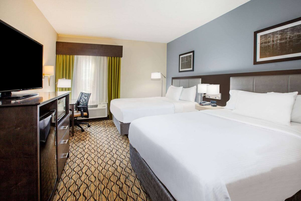 A hotel room with two beds, a desk with a television, a chair, and a patterned carpet.