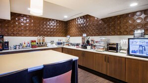 A modern kitchen with a central island, wooden cabinets, and a variety of appliances and food items. - Wingate by Wyndham Roseville/Detroit (Roseville)