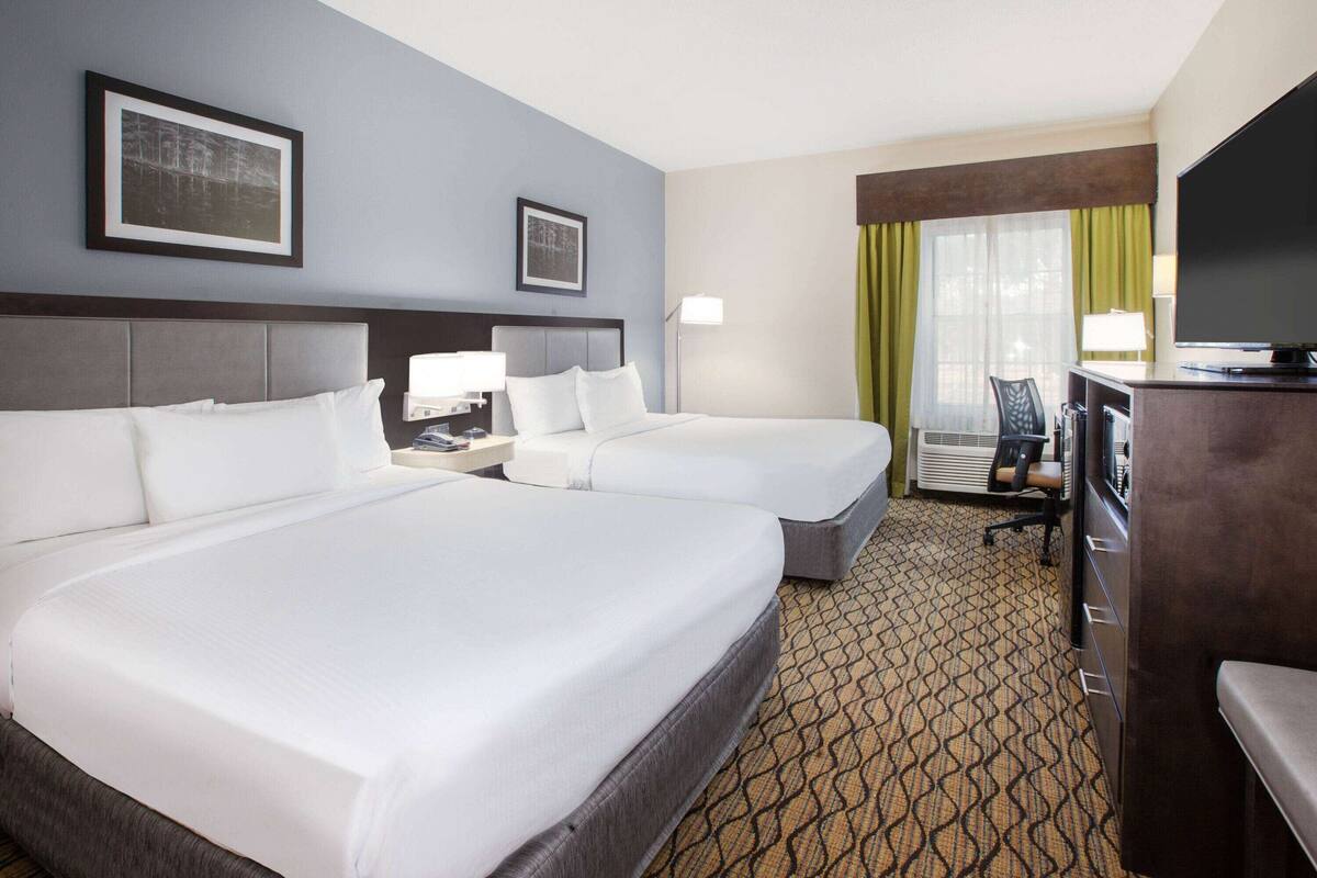 A hotel room with two beds, a desk, a chair, a television, and a window with curtains.