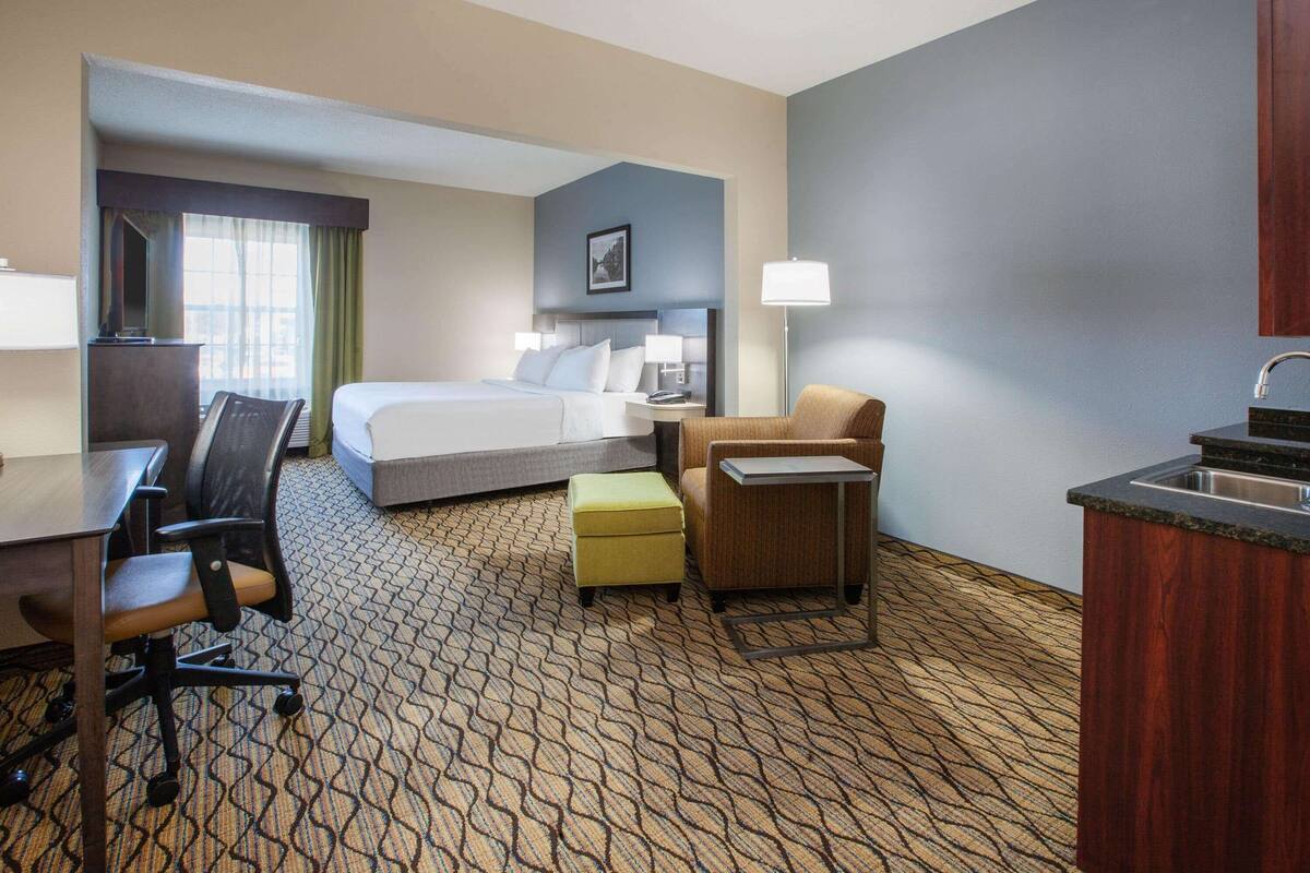 A hotel room with a bed, desk, chair, and kitchenette.