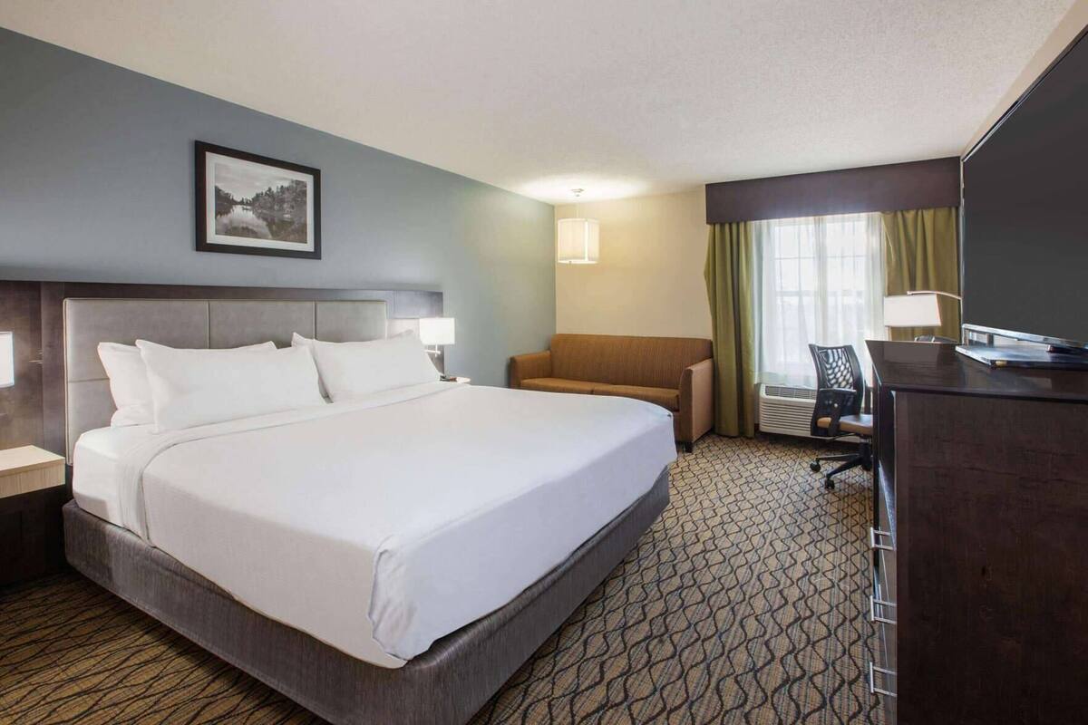A hotel room with a large bed, a desk, a chair, and a picture on the wall.