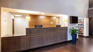 A reception desk with a wooden panel design, a potted plant, and a television mounted on the wall. - Wingate by Wyndham Roseville/Detroit (Roseville)