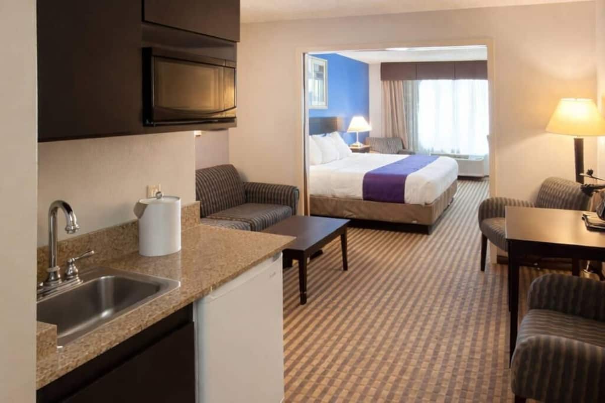 A hotel room with a kitchenette, a bed, a seating area, and a view of the outside.