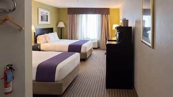 A hotel room with two beds, a desk, a fire extinguisher, and a framed picture on the wall.
