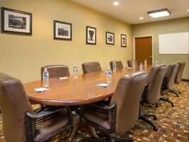 Un salón de conferencias con una gran mesa de madera, sillas de cuero marrón, botellas de agua y fotografías enmarcadas en la pared.