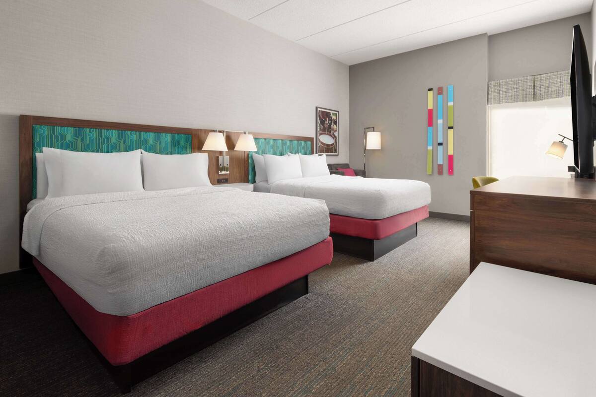 A hotel room with two beds, a desk, and a TV.