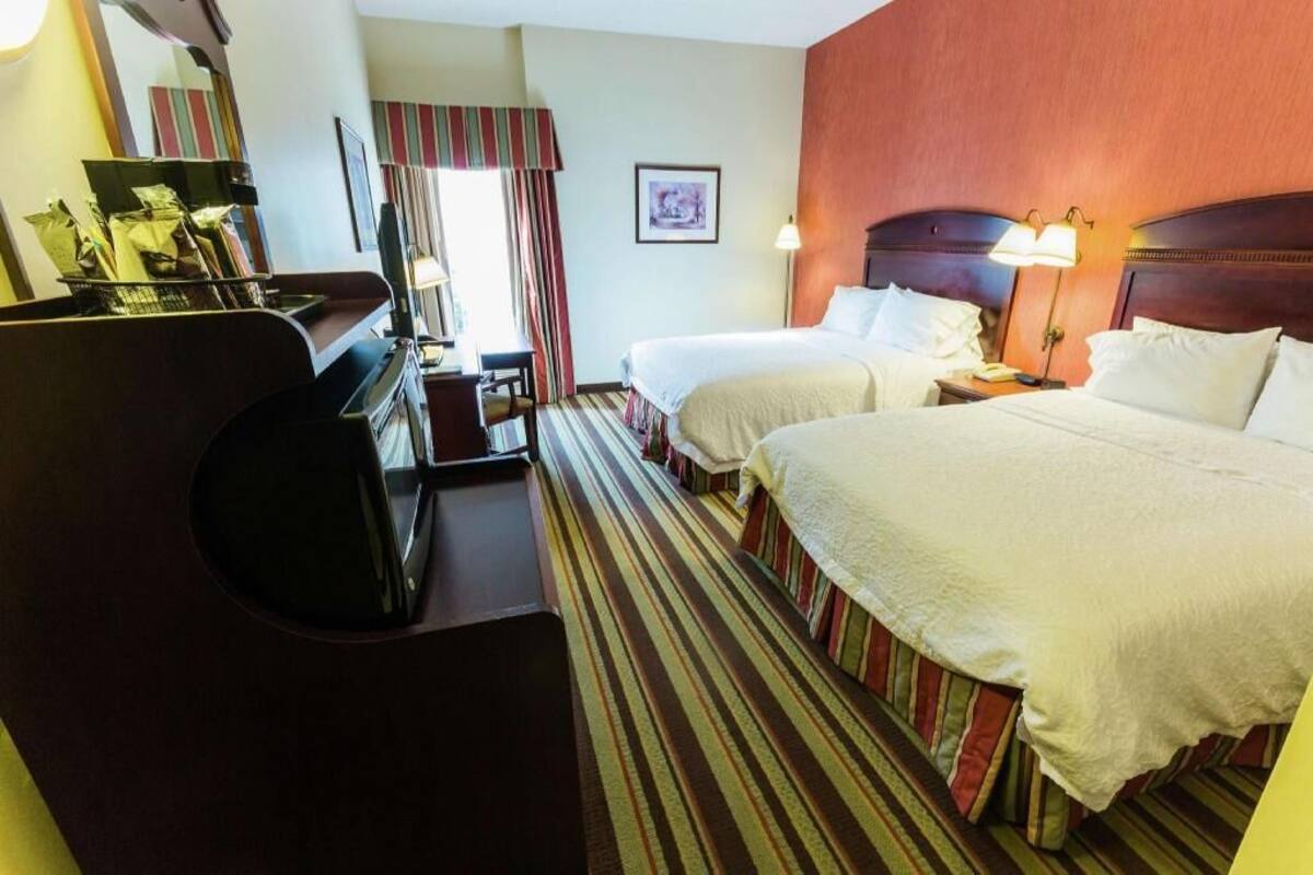 A hotel room with two beds, a desk, a chair, a television, and a window with curtains.