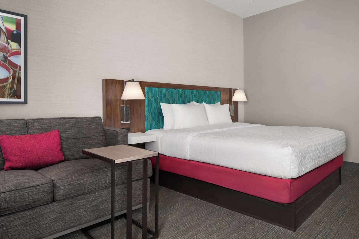 A hotel room with a bed, a nightstand, a table, a sofa, and a wall-mounted lamp.