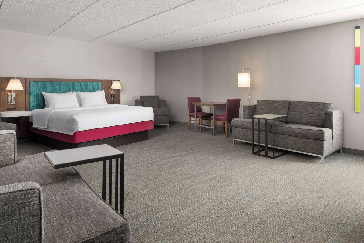 A hotel room with a bed, a sofa, a small table, and two chairs.