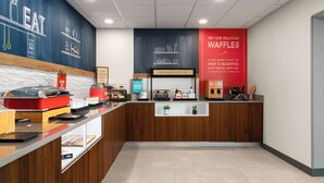 A bakery counter with a chalkboard menu, a sign for waffles, and a 'Happy Breakfast Starts Here' sign. - Hampton Inn Sturbridge (Sturbridge)
