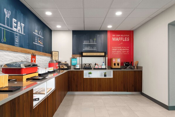 A bakery counter with a chalkboard menu, a sign for waffles, and a 'Happy Breakfast Starts Here' sign.