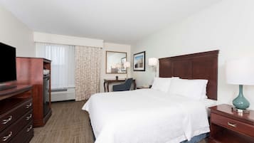 A hotel room with a large bed, a desk, a chair, a television, and a dresser.