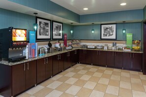 A hotel kitchen with a coffee machine, a food display, and a beverage dispenser.