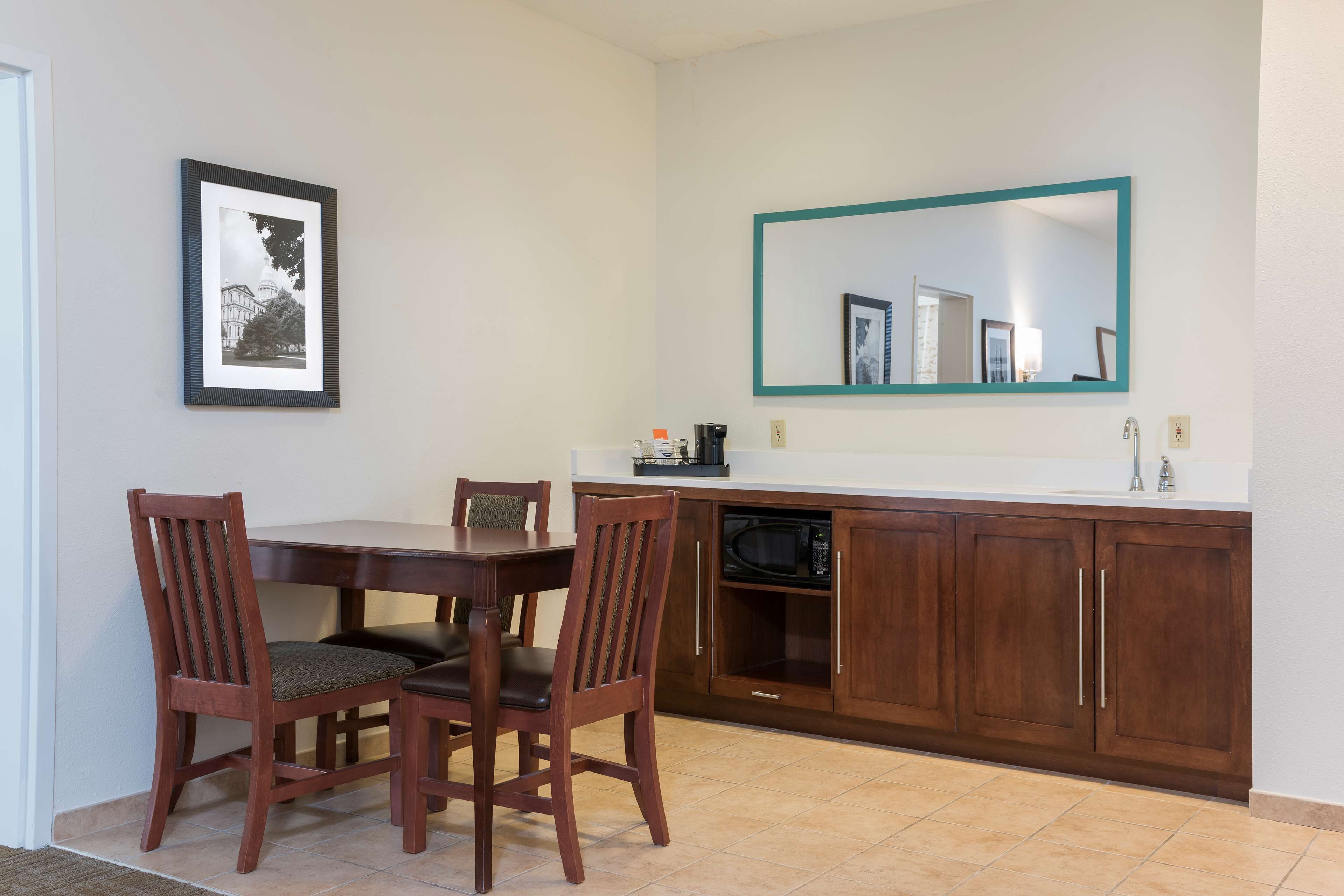 A dining area with a wooden table and chairs, a framed picture on the wall, a microwave, and a cabinet with a mirror above it.