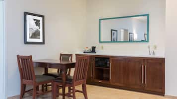 Un comedor con una mesa y sillas de madera, un cuadro en la pared, un microondas y un mueble con un espejo encima.