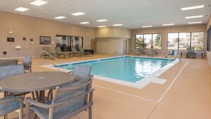 Ein Hallenbad mit Liegestühlen und Tischen, einem Sprungverbotsschild und Blick ins Freie.