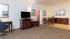 Ein Hotelzimmer mit Flachbildfernseher, Schreibtisch mit Stuhl, Essbereich mit Tisch und Stühlen sowie Küchenzeile mit Schränken und Mikrowelle.