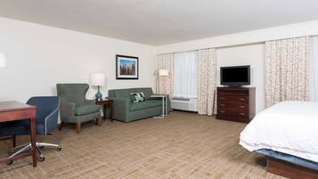 A hotel room with a bed, a desk, a chair, a sofa, a TV, a dresser, and a picture on the wall.