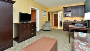 Una habitación de hotel compacta con televisión en una cómoda, un sofá, una mesa de comedor y una kitchenette.