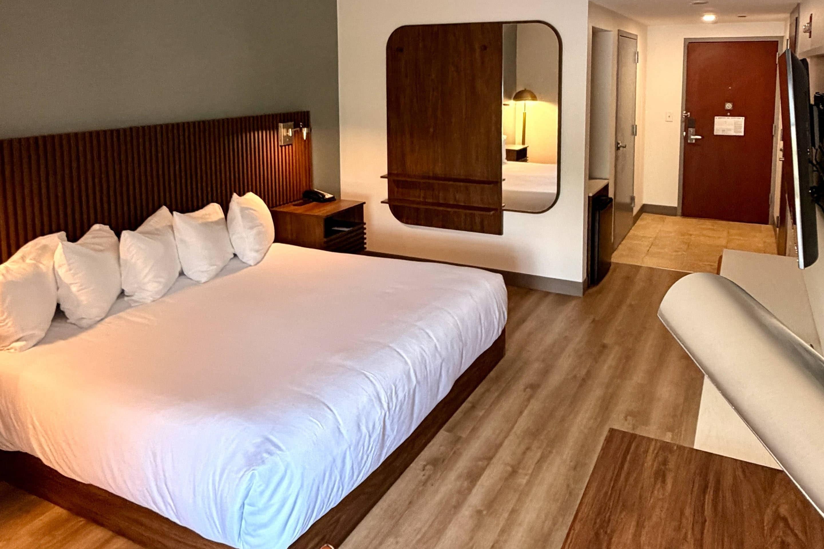 A hotel room with a large bed, a bedside table, a mirror, a door, and a small seating area.