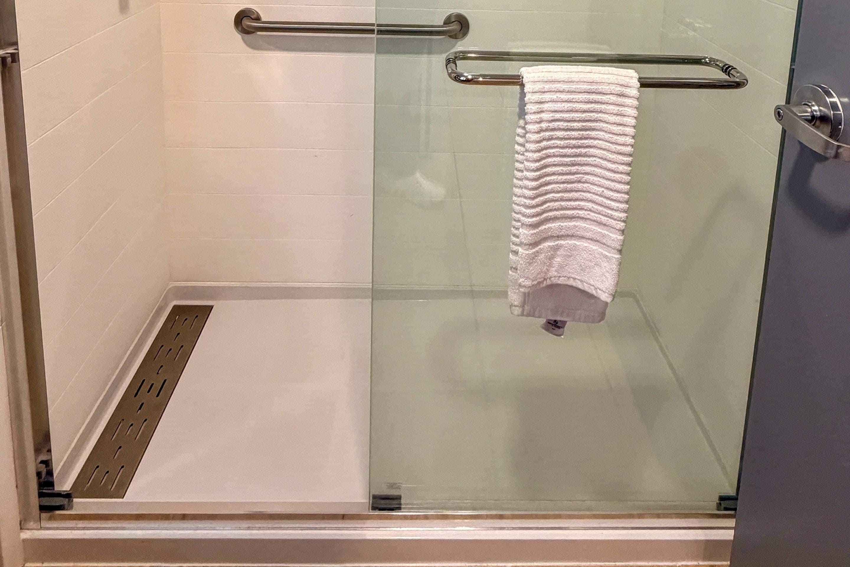 Un box de ducha con paredes de vidrio, una barra de apoyo metálica y una toalla blanca colgada en la pared.