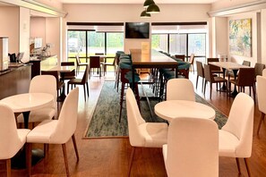 Un comedor amplio con varias mesas y sillas, una barra y un ventanal con vistas al exterior.