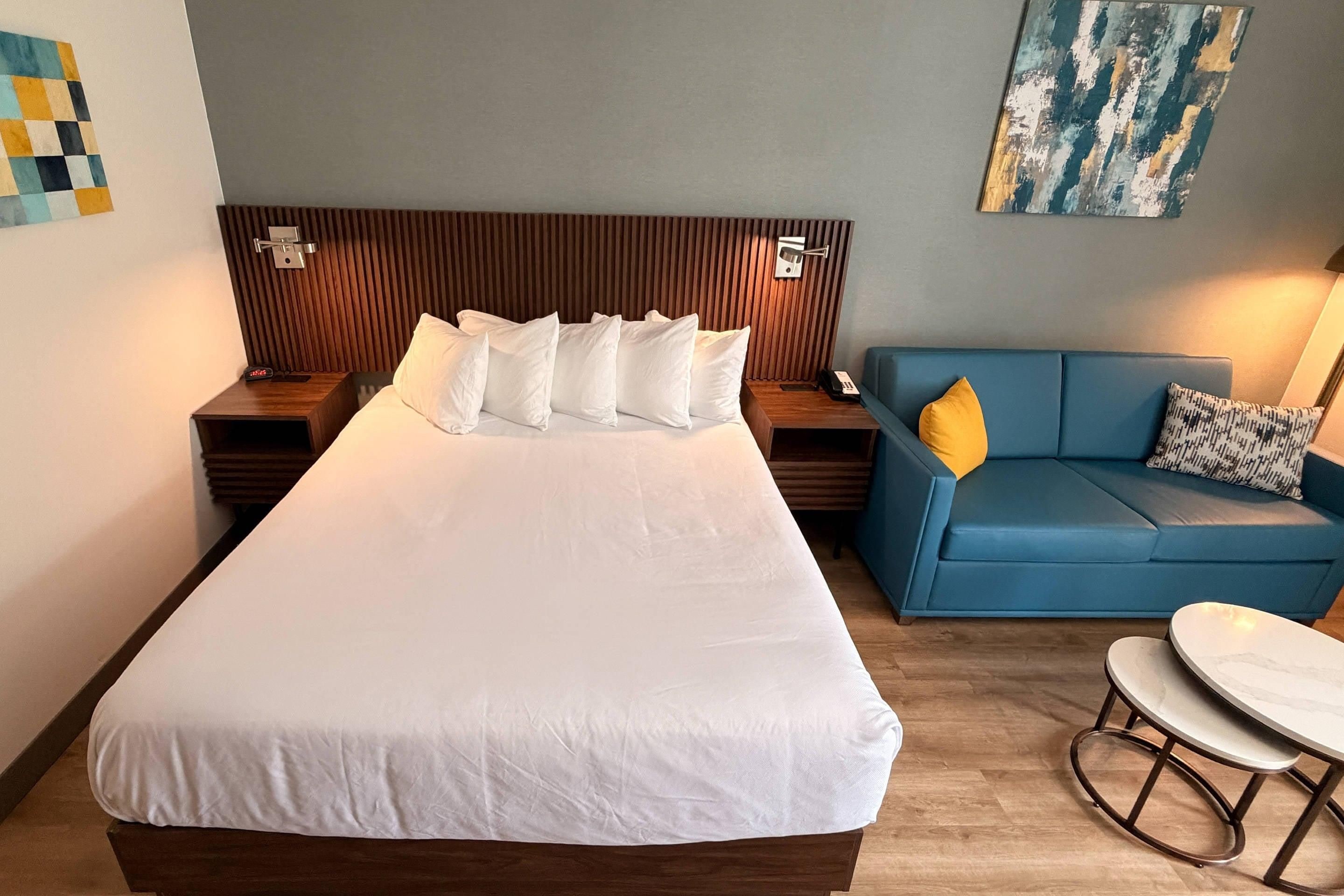 A hotel room with a large bed, a blue sofa, a small table, and a painting on the wall.