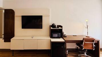 A modern office space with a flat-screen TV mounted on the wall, a desk with a computer, a microwave, and a chair.
