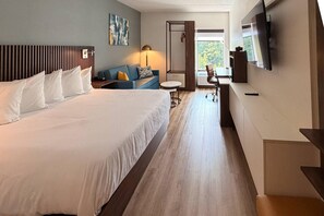 A hotel room with a large bed, a sofa, a desk, and a TV.