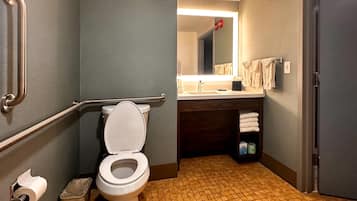 A bathroom with a toilet, handrails, a sink, and a mirror.