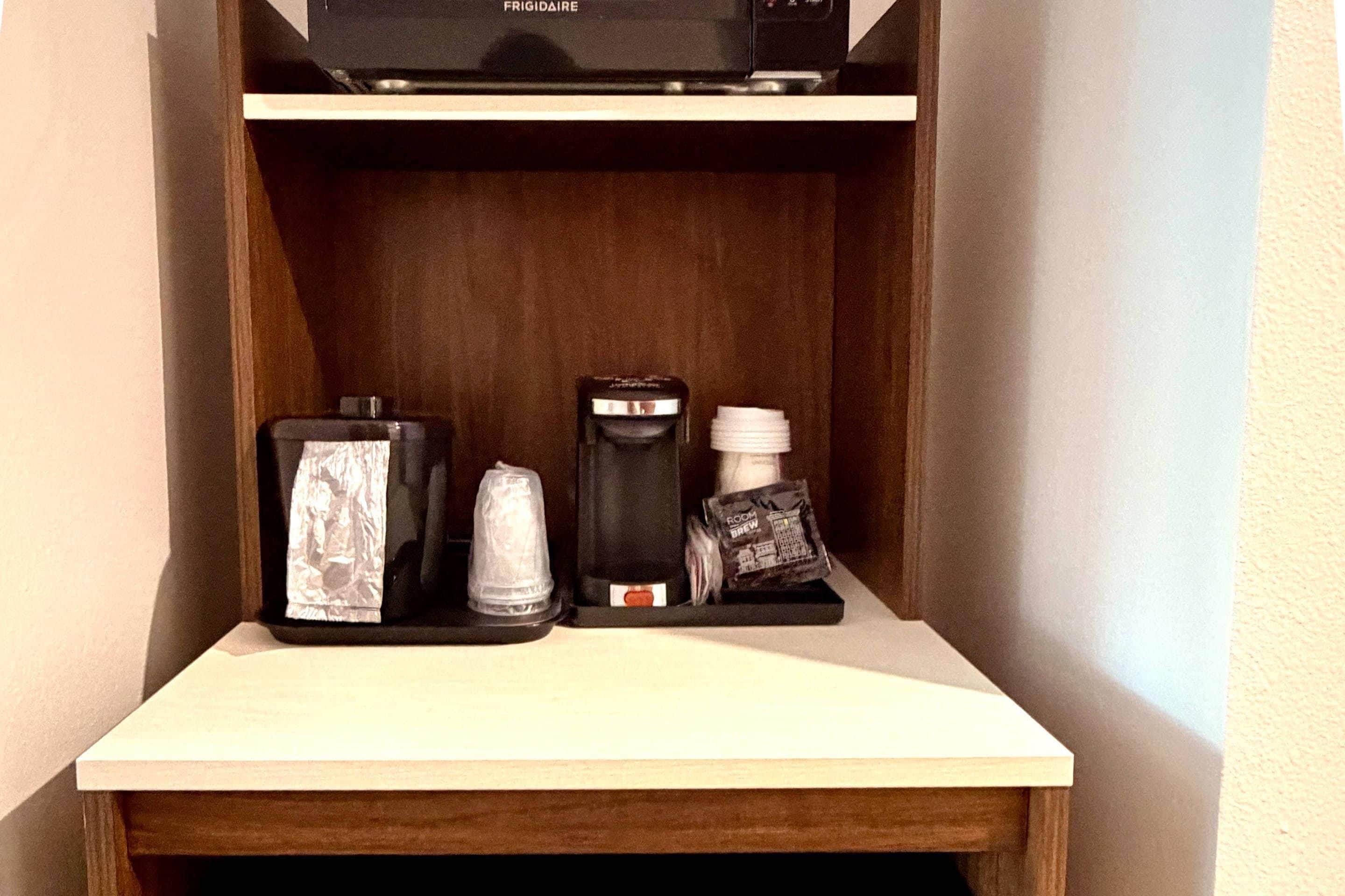 A small wooden shelf with a coffee maker, a glass container, and a coffee pod holder.