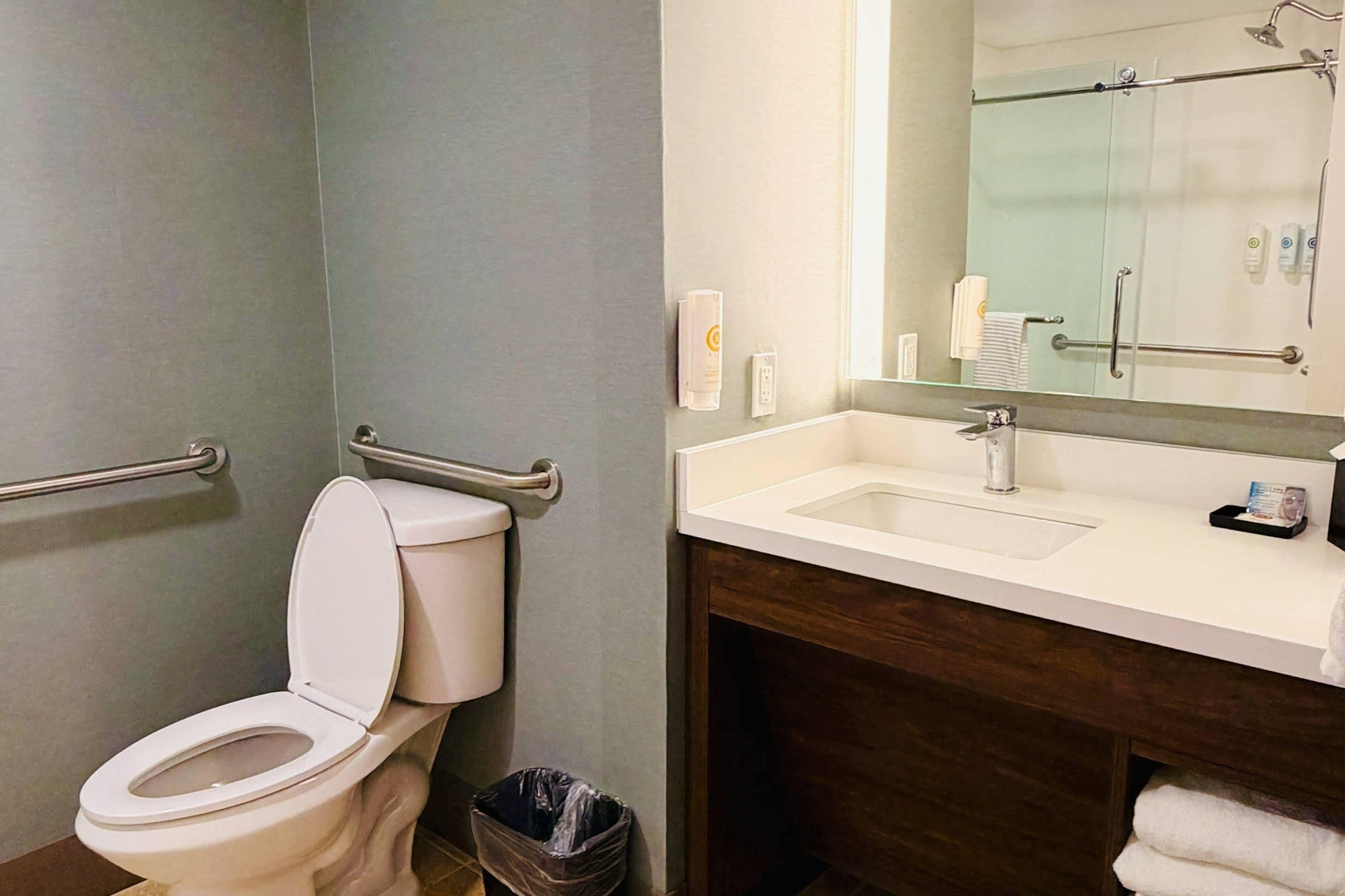Un baño con inodoro, lavamanos, espejo y un cubo de basura.