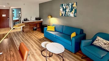 A modern living room with a blue sofa, two round tables, a coffee machine, and a painting on the wall.