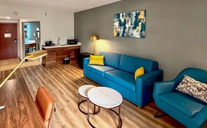 Una sala de estar moderna con un sofá azul, dos mesas redondas, una cafetera y un cuadro en la pared.