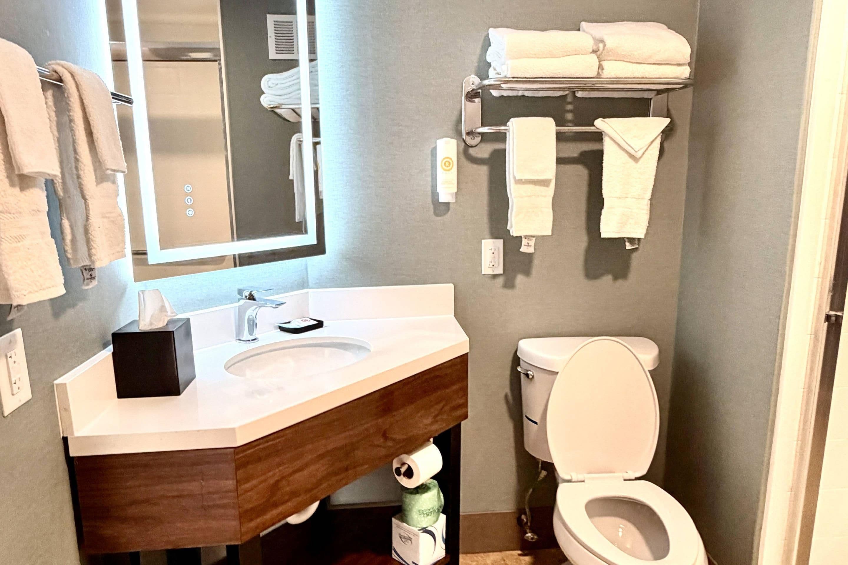 A bathroom with a wooden vanity, a mirror, a sink, a toilet, and a towel rack with towels.