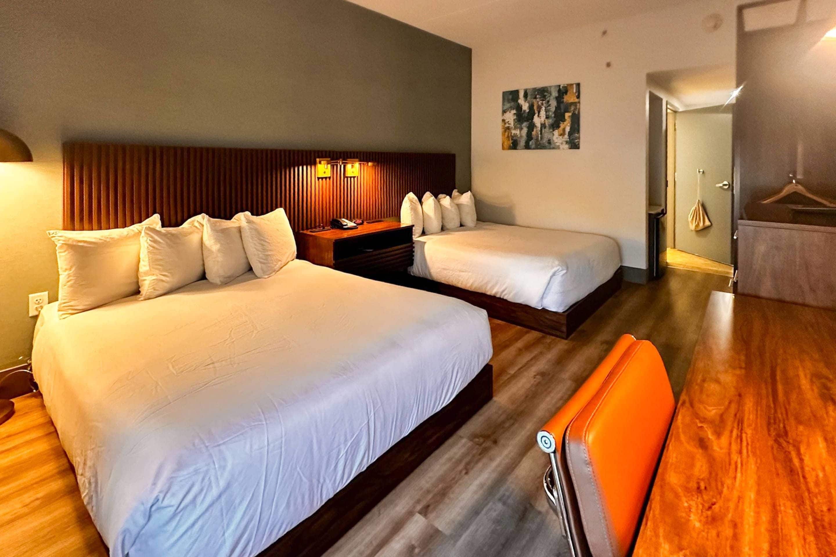 A hotel room with two beds, a wooden floor, a desk, and a chair.