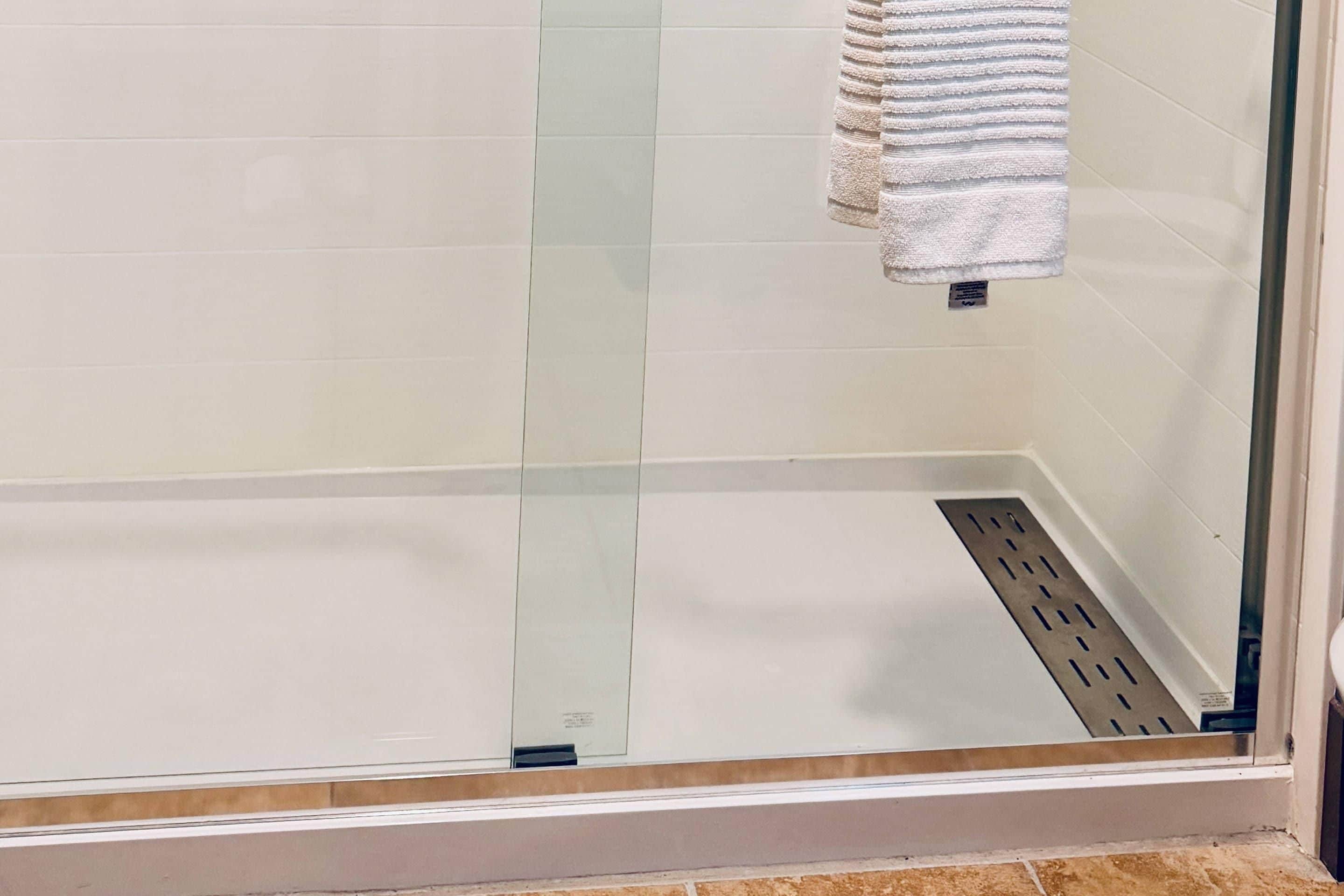 A shower area with a glass door, a towel hanging on the wall, and a drain in the floor.