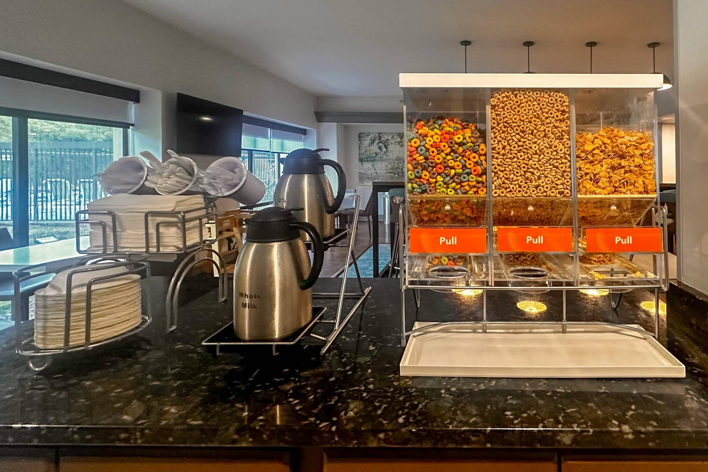 A kitchen counter with a coffee maker, a kettle, and a pull station for snacks.