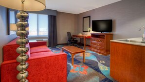 A hotel room with a red sofa, a wooden desk, a television, and a kitchen area.