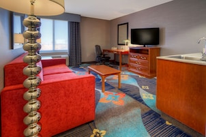 A hotel room with a red sofa, a wooden desk, a television, and a kitchen area.