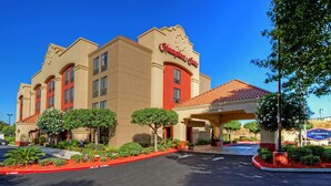 A Hampton Inn hotel with a red and beige facade, a covered entrance, and landscaped parking area.