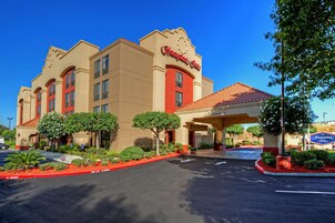 A Hampton Inn hotel with a red and beige facade, a covered entrance, and landscaped parking area.
