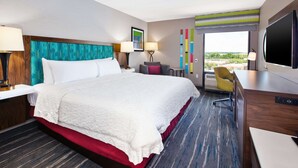A hotel room with a large bed, a desk with a flat-screen TV, a chair, and a view of the outdoors. - Hampton Inn College Park (College Park)