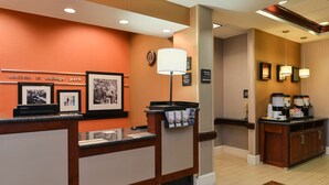A reception area with a counter, framed pictures, a clock, and a coffee station. - Hampton Inn College Park (College Park)