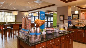 A hotel breakfast area with a buffet setup, including various food containers and a coffee station. - Hampton Inn College Park (College Park)